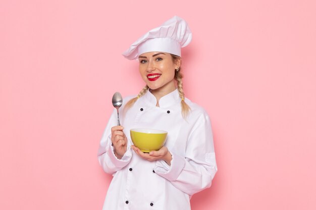 Vue de face jeune femme cuisinier en costume de cuisinier blanc tenant une plaque verte avec sourire sur l'espace rose cook