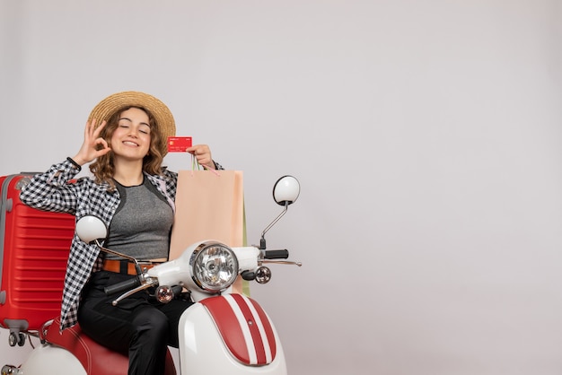 Vue de face jeune femme sur cyclomoteur holding card faisant signe ok