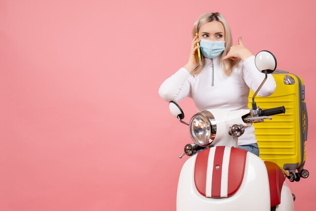 Vue de face jeune femme sur cyclomoteur avec valise jaune appelant quelqu'un avec son téléphone