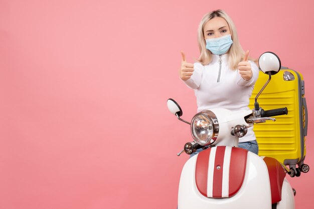 Vue de face jeune femme sur cyclomoteur avec valise jaune faisant signe de pouce en l'air