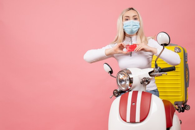 Vue de face jeune femme sur cyclomoteur avec valise jaune holding card