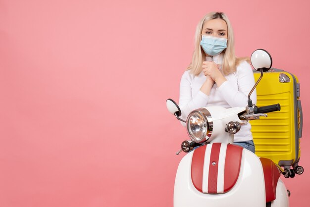 Vue de face jeune femme sur cyclomoteur avec valise jaune mains jointes