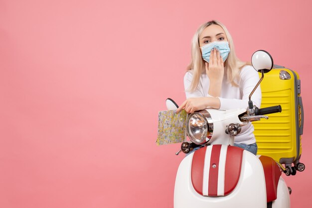 Vue de face jeune femme sur cyclomoteur avec valise jaune mettant la main sur sa bouche