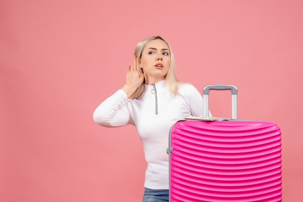 Vue de face jeune femme debout derrière une valise rose en écoutant quelque chose