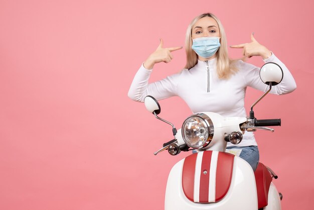 Vue de face jeune femme debout près de cyclomoteur pointant sur son masque