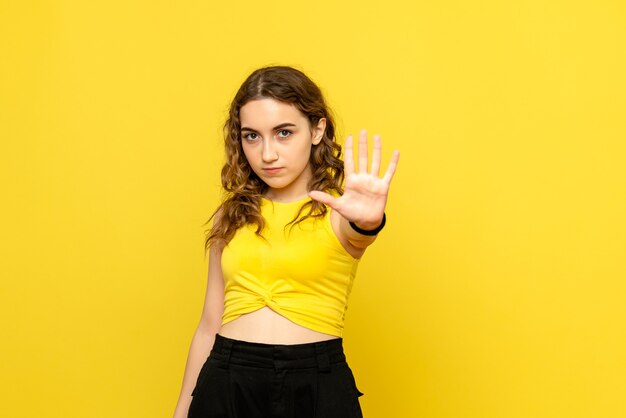 Vue de face de la jeune femme demandant de s'arrêter sur le mur jaune