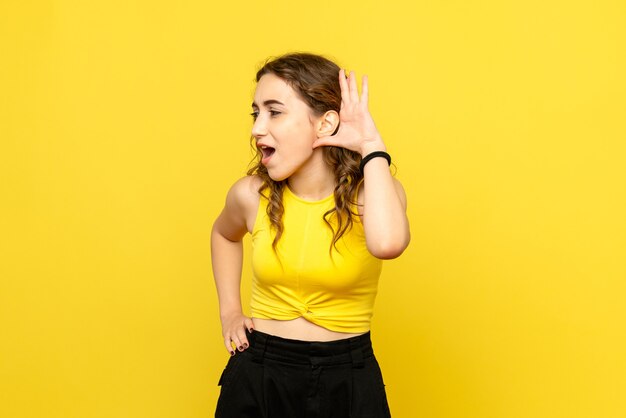 Vue de face de la jeune femme écoutant attentivement sur le mur jaune