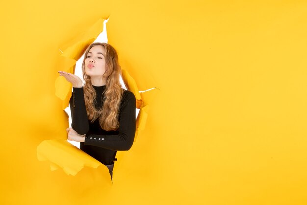 Vue de face jeune femme envoyant des baisers sur un mur déchiré jaune