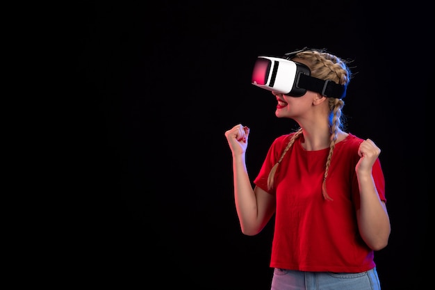 Vue de face d'une jeune femme excitée jouant à la réalité virtuelle sur une technologie de jeu visuel à ultrasons sombres