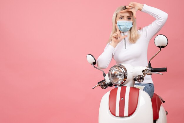 Vue de face jeune femme faisant signe de la caméra debout près de cyclomoteur