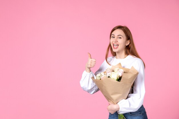 Vue de face jeune femme avec des fleurs comme jour de la femme présente sur fond rose horizontal féminin mars date sensuelle égalité rose amour