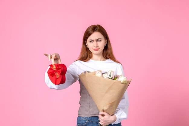 Vue de face jeune femme avec des fleurs et présente comme cadeau de jour de la femme sur fond rose l'égalité de mars horizontale date féminine rose femme amour