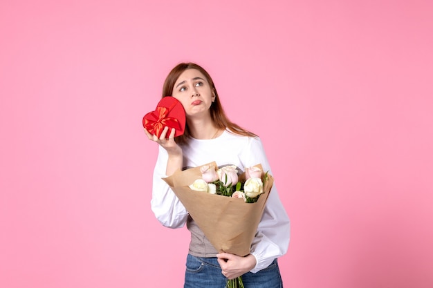 Vue de face jeune femme avec des fleurs et présente comme cadeau de jour de la femme sur fond rose l'égalité de mars horizontale féminine rose femme amour sensuel