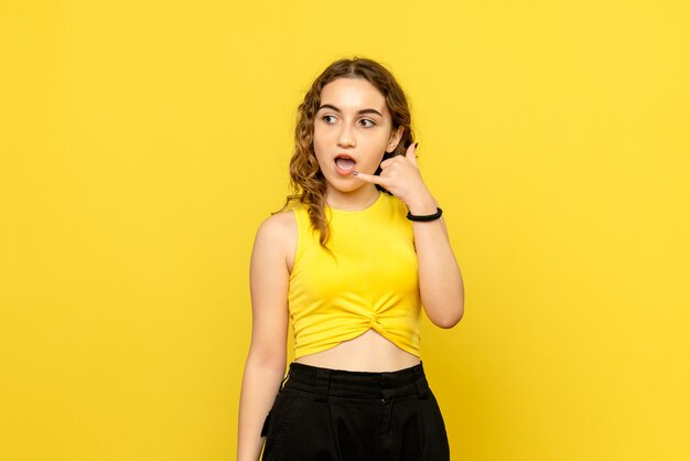 Vue de face de la jeune femme imitant l'appel téléphonique sur le mur jaune