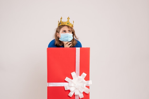 Vue de face d'une jeune femme à l'intérieur d'une boîte-cadeau en masque sur un mur blanc