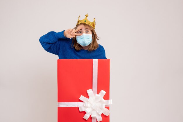 Vue de face d'une jeune femme à l'intérieur d'une boîte-cadeau en masque sur un mur blanc