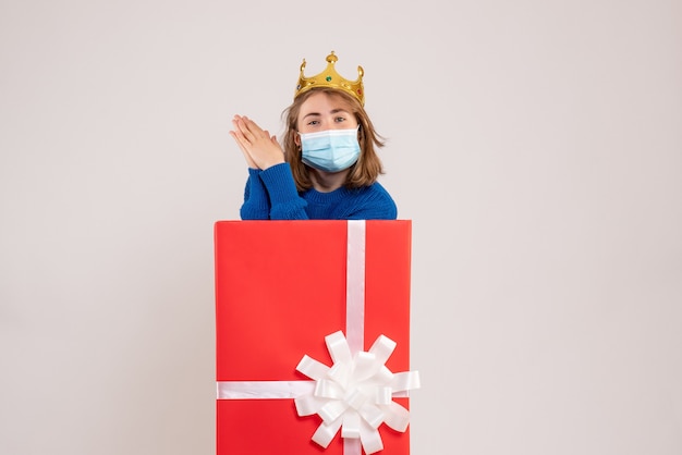 Vue de face d'une jeune femme à l'intérieur d'une boîte-cadeau en masque sur un mur blanc