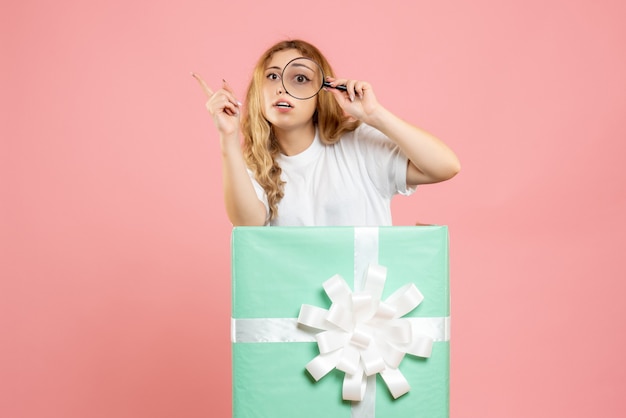 Photo gratuite vue de face jeune femme à l'intérieur de la boîte présente bleu à l'aide de la loupe