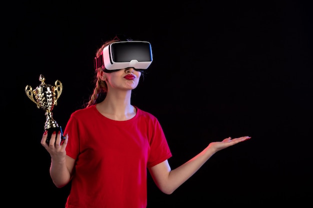 Vue de face d'une jeune femme jouant au vr avec la coupe du vainqueur sur un jeu de technologie visuelle d'un bureau sombre