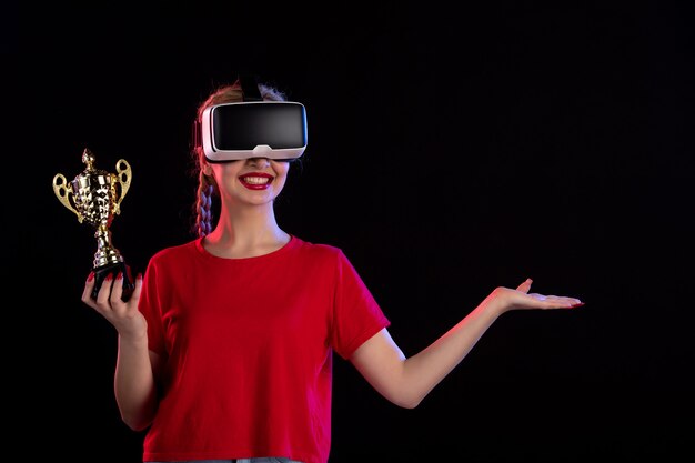 Vue de face d'une jeune femme jouant à la réalité virtuelle et gagnant la coupe sur un mur sombre