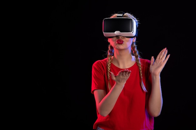 Vue de face d'une jeune femme jouant à la réalité virtuelle sur un mur sombre