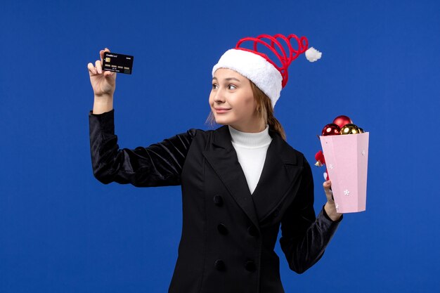 Vue de face jeune femme avec des jouets d'arbre et carte bancaire sur le mur bleu émotion vacances de nouvel an