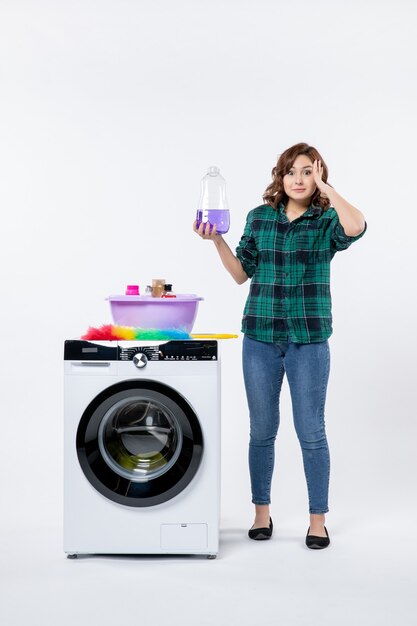 Vue de face de la jeune femme avec lave-linge sur mur blanc