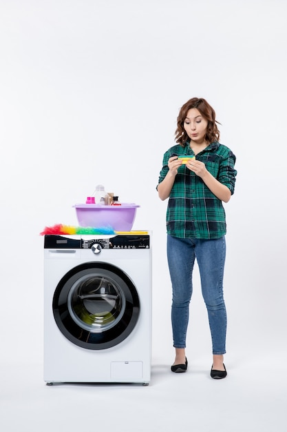 Vue de face de la jeune femme avec lave-linge sur mur blanc