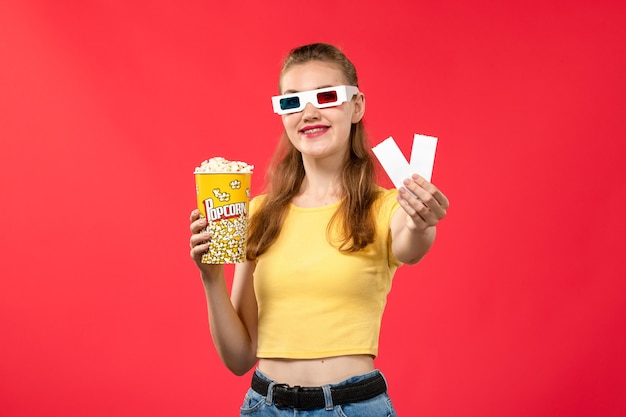 Vue de face jeune femme en d lunettes de soleil au cinéma tenant des billets et du pop-corn sur mur rouge cinéma cinéma couleur féminine