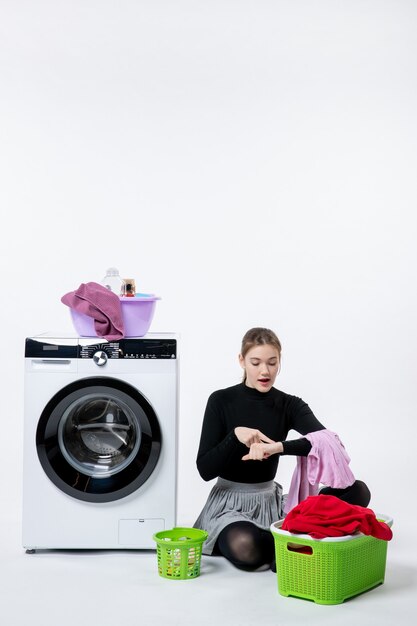 Vue de face d'une jeune femme avec une machine à laver pliant des vêtements sales sur un mur blanc