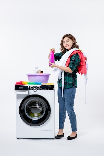 Vue de face d'une jeune femme avec une machine à laver préparant des vêtements sur un mur blanc