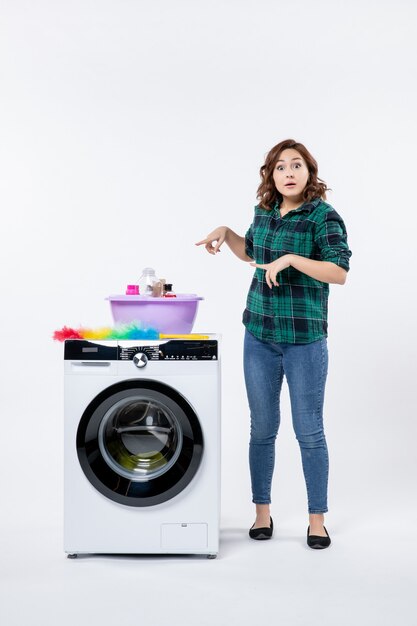 Vue de face jeune femme avec machine à laver et shampoings sur mur blanc