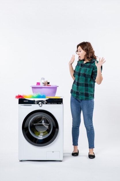 Vue de face jeune femme avec machine à laver et shampoings sur mur blanc