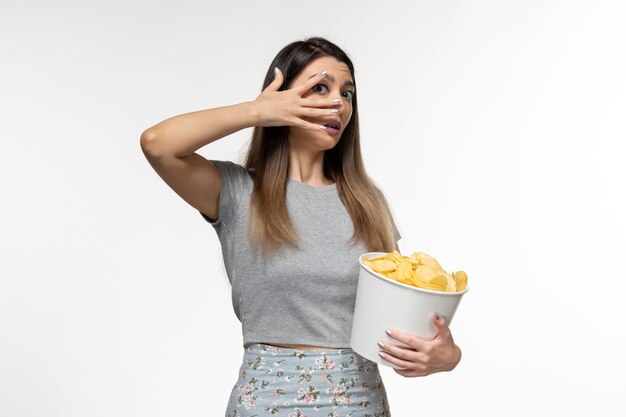 Vue de face jeune femme mangeant des chips de pomme de terre regarder un film sur la surface blanche légère