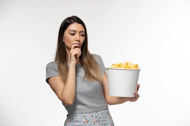 Vue de face jeune femme mangeant des chips de pomme de terre regarder un film sur la surface blanche légère