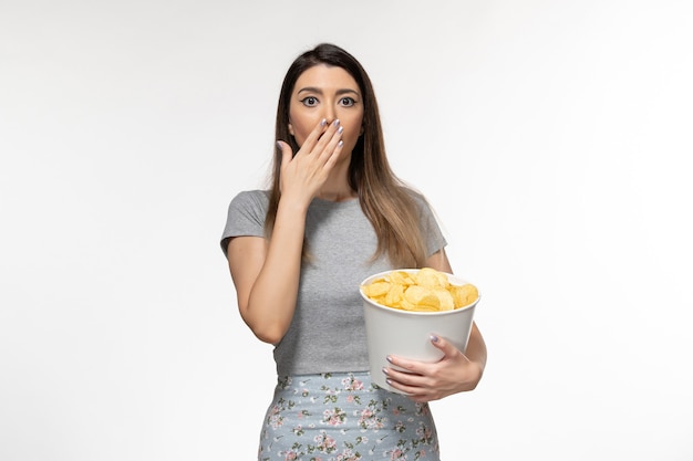Vue de face jeune femme mangeant des chips de pomme de terre regarder un film sur la surface blanche