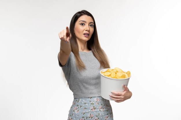 Vue de face jeune femme mangeant des chips de pomme de terre regarder un film sur la surface blanche