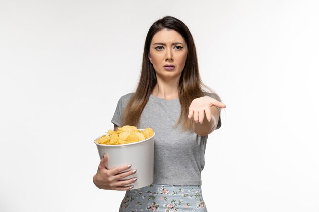 Vue de face jeune femme mangeant des cips et regarder un film sur le bureau blanc