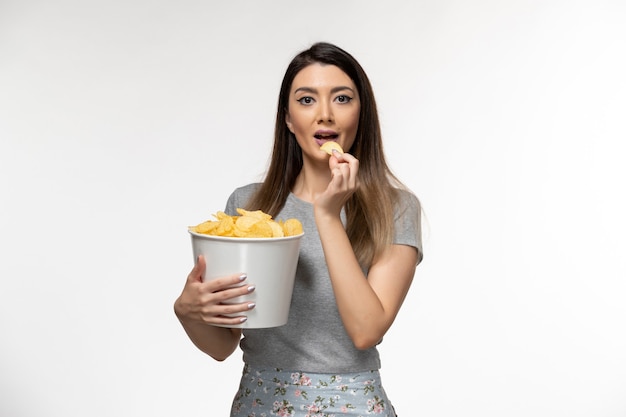 Vue de face jeune femme mangeant des cips et regarder un film sur une surface blanche