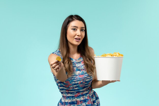 Vue de face jeune femme mangeant des cips et regarder un film sur la surface bleue