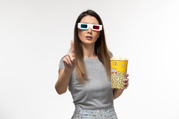 Vue de face jeune femme mangeant du pop-corn et regarder un film dans des lunettes de soleil sur un bureau blanc