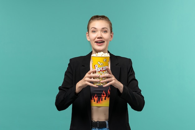 Vue de face jeune femme mangeant du pop-corn et regarder un film sur la surface bleue