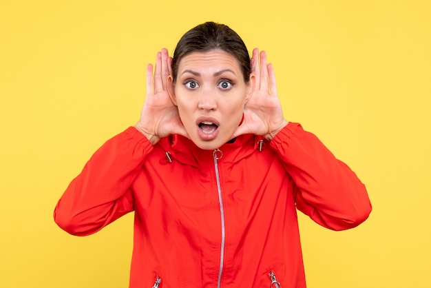 Vue de face jeune femme en manteau rouge à l'écoute sur fond jaune