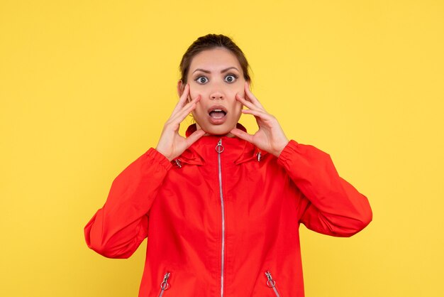 Vue de face jeune femme en manteau rouge sur fond jaune