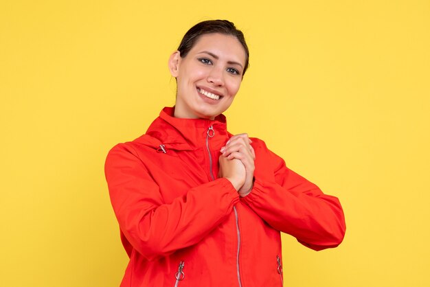 Vue de face jeune femme en manteau rouge avec visage heureux sur fond jaune