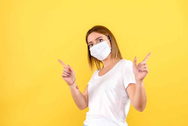 Vue de face de la jeune femme en masque sur un mur jaune