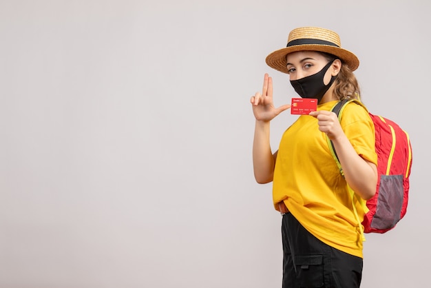 Vue de face jeune femme avec masque noir tenant une carte faisant un pistolet à doigt