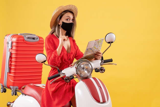 Vue de face jeune femme avec masque noir tenant une carte surprenante avec une idée près d'un cyclomoteur