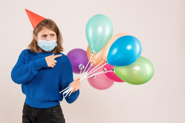 Vue de face jeune femme en masque stérile tenant des ballons colorés