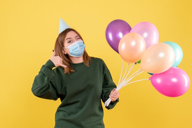 Vue de face jeune femme en masque tenant des ballons colorés